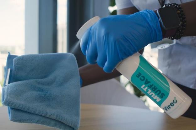 A commercial contract cleaning employee using multi surface spray to clean a table.