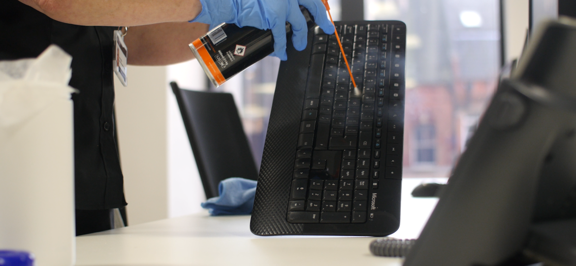 Professional cleaner carrying out office IT cleaning on a computer keyboard using specialist cleaning equipment.